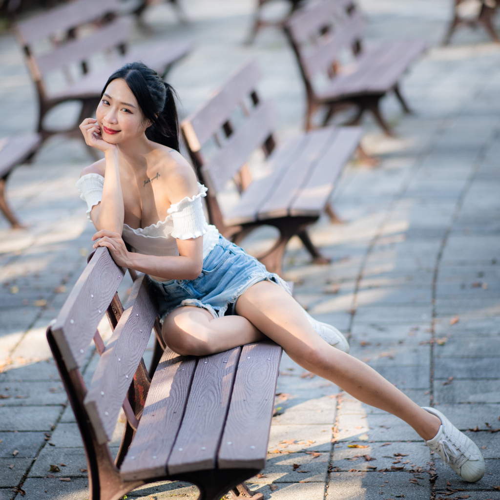 Милая девушка азиатка сидит на лавке в парке