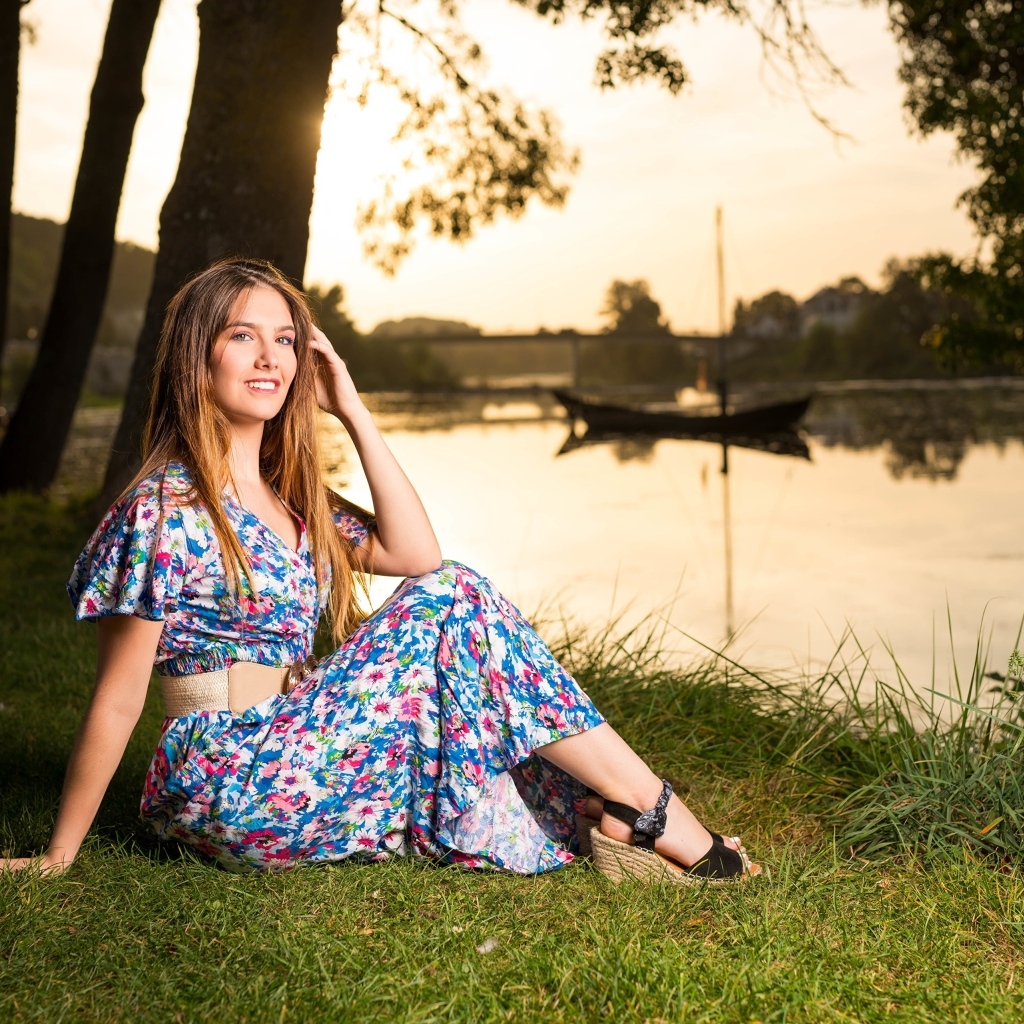 Милая девушка в платье сидит на берегу реки в парке