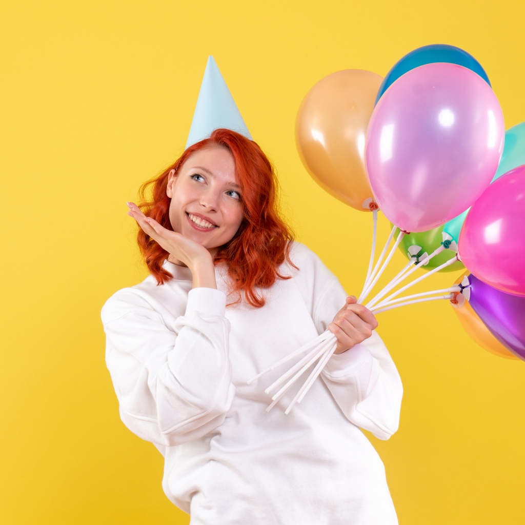 Милая рыжеволосая девушка с шариками на желтом фоне