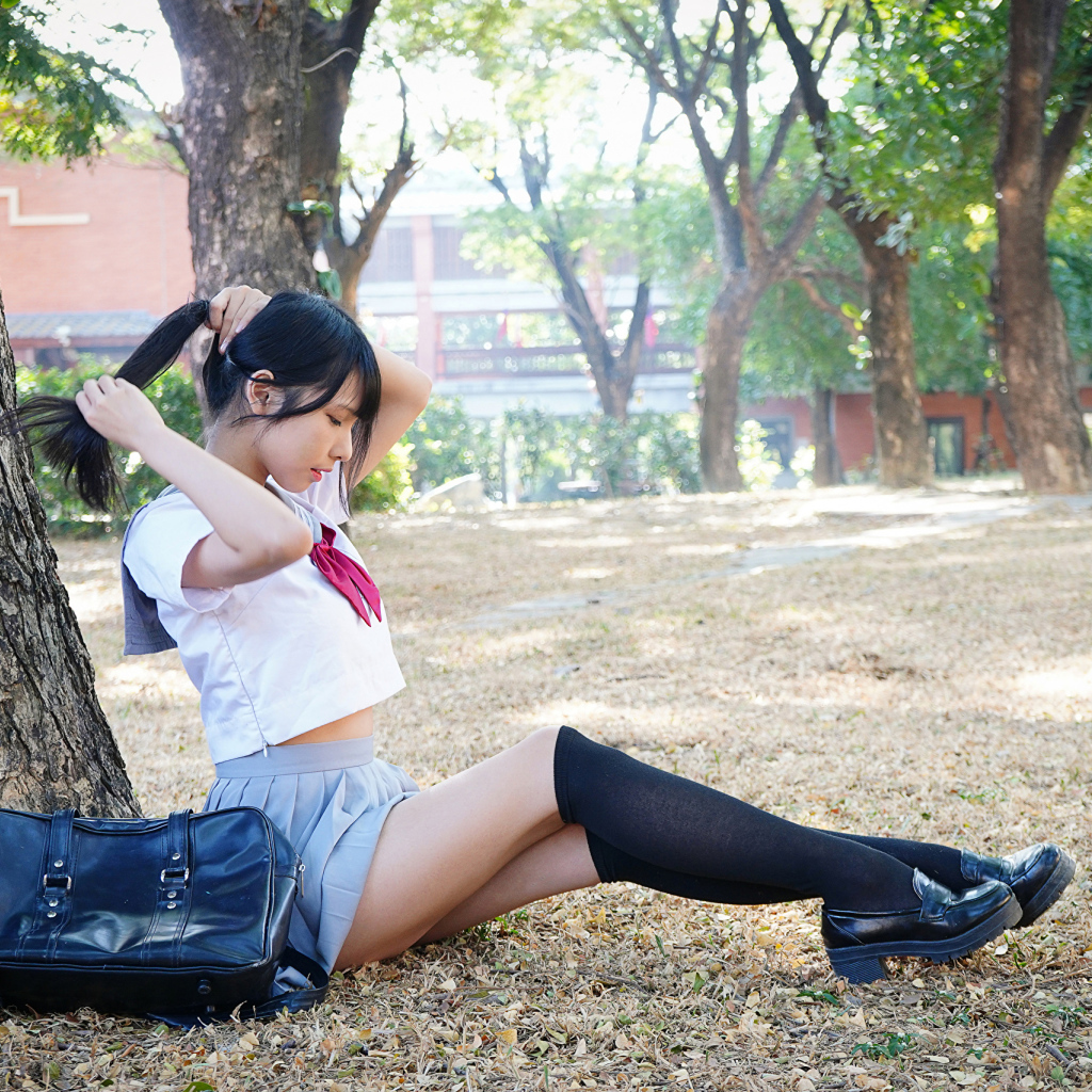 Милая молодая девушка студентка сидит под деревом в парке