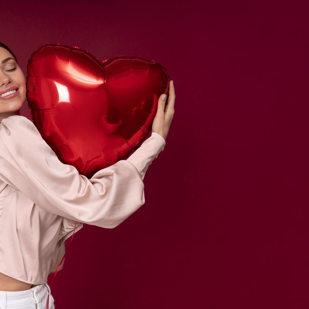 Девушка держит шарик в форме сердца на красном фоне