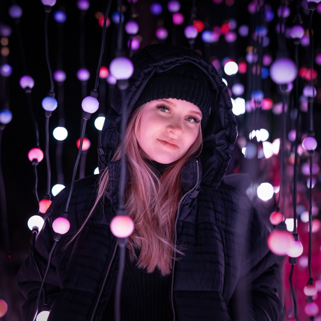Девушка в черной куртке у светящейся гирлянды