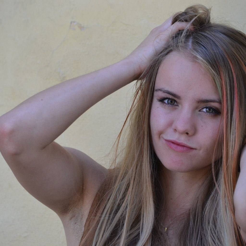 Девушка с руками в волосах у стены