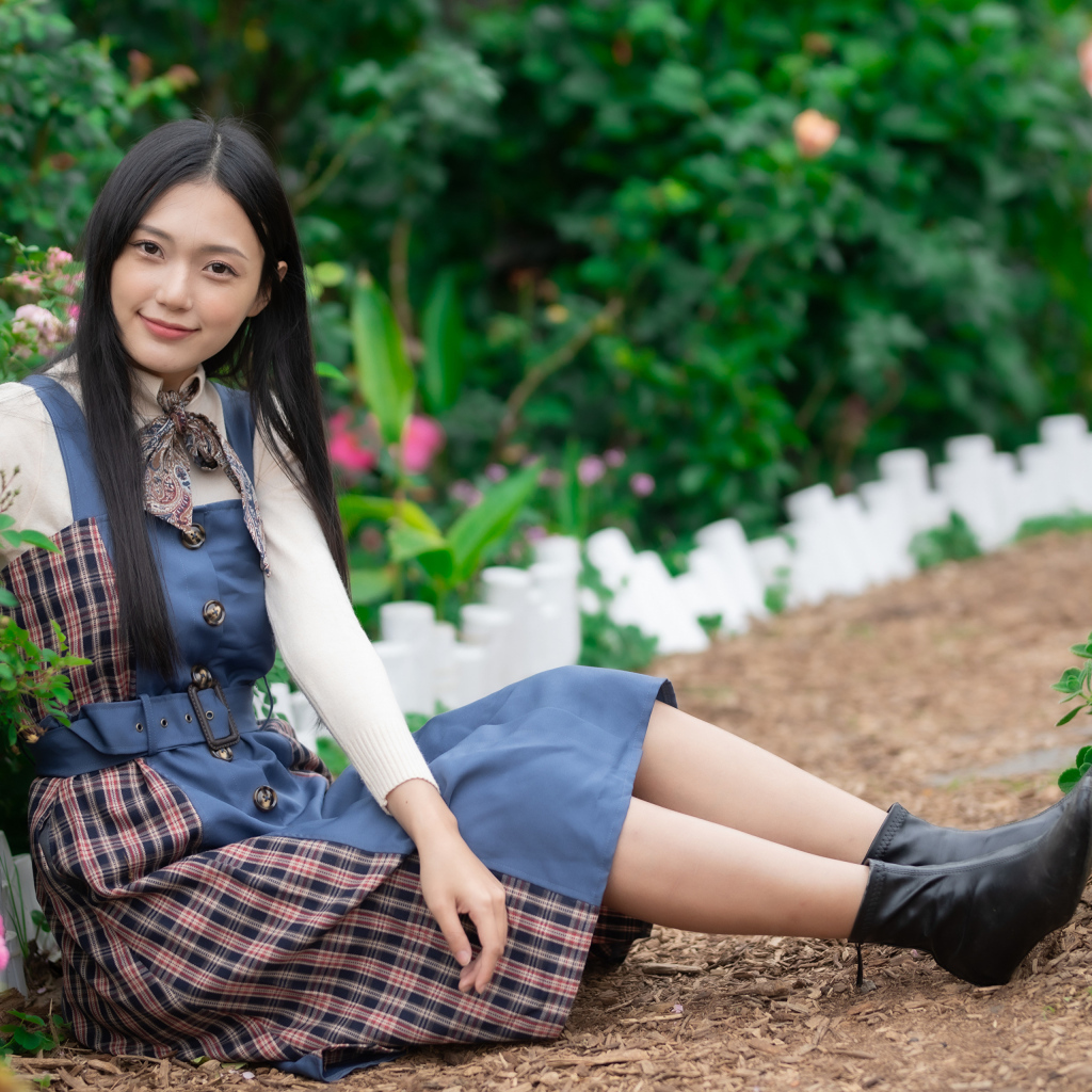 Настоящая молодая азиатка сидит на земле у клумбы