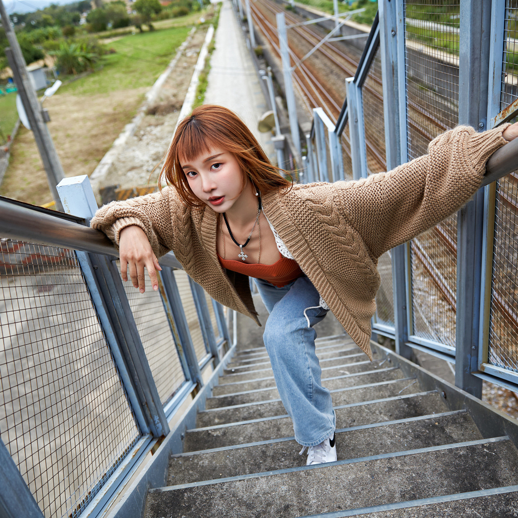 Рыжеволосая азиатка в кофте стоит на ступеньках