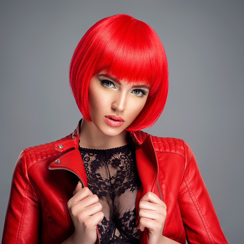 Рыжеволосая девушка с короткой стрижкой в красной кожаной куртке на сером фоне