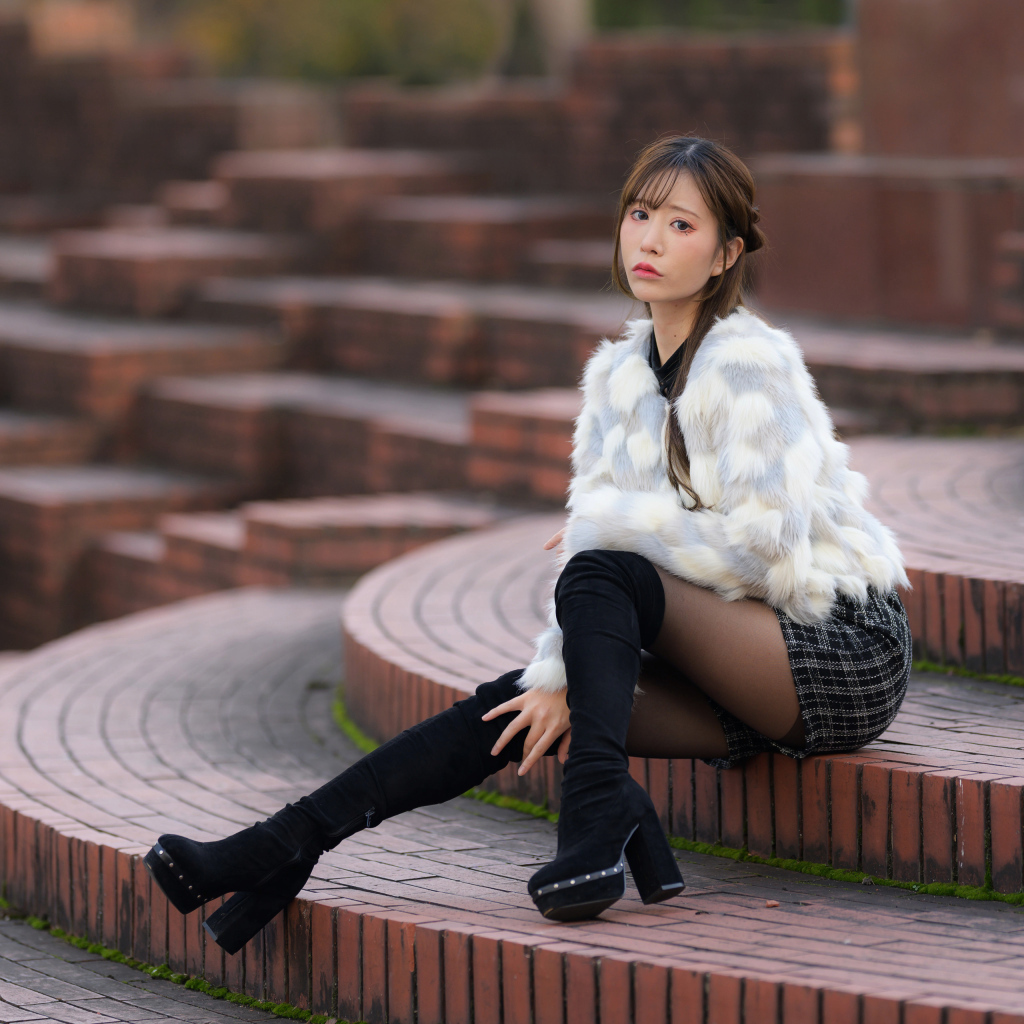 Грустная азиатка в шубе сидит на ступеньках