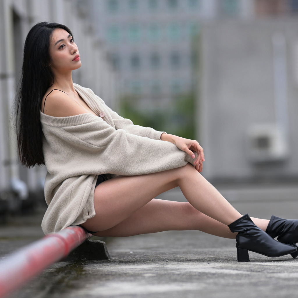 Грустная азиатка в теплой кофте сидит на трубе