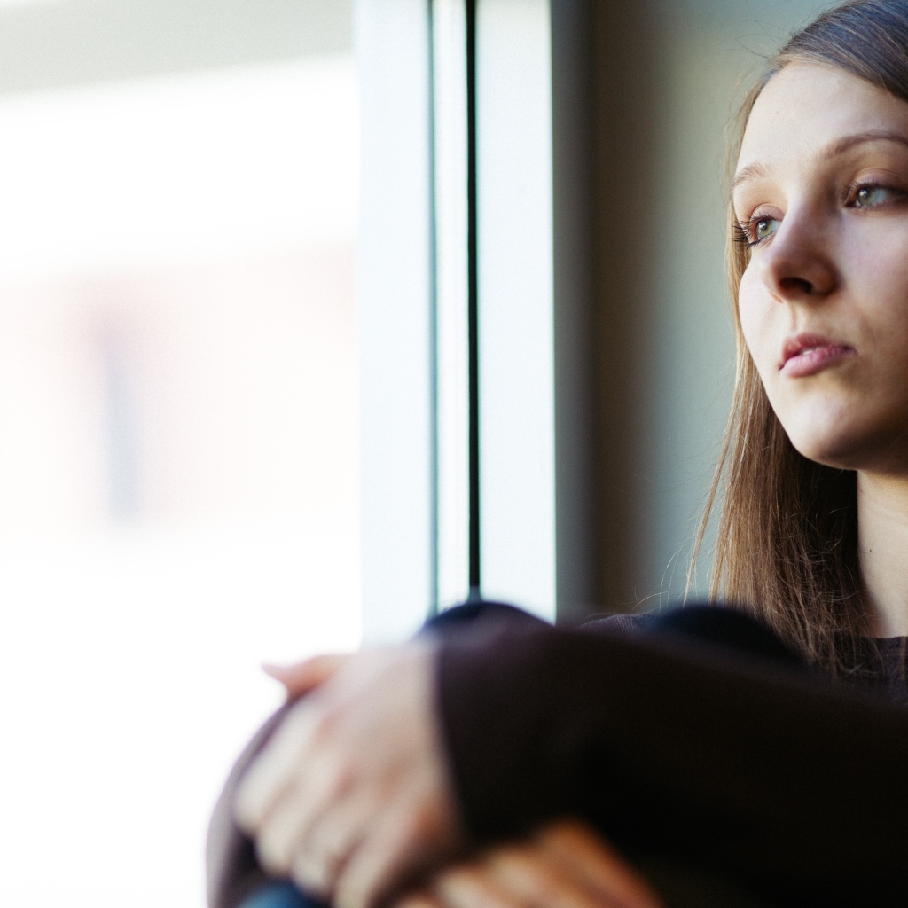 Грустная девушка сидит у окна