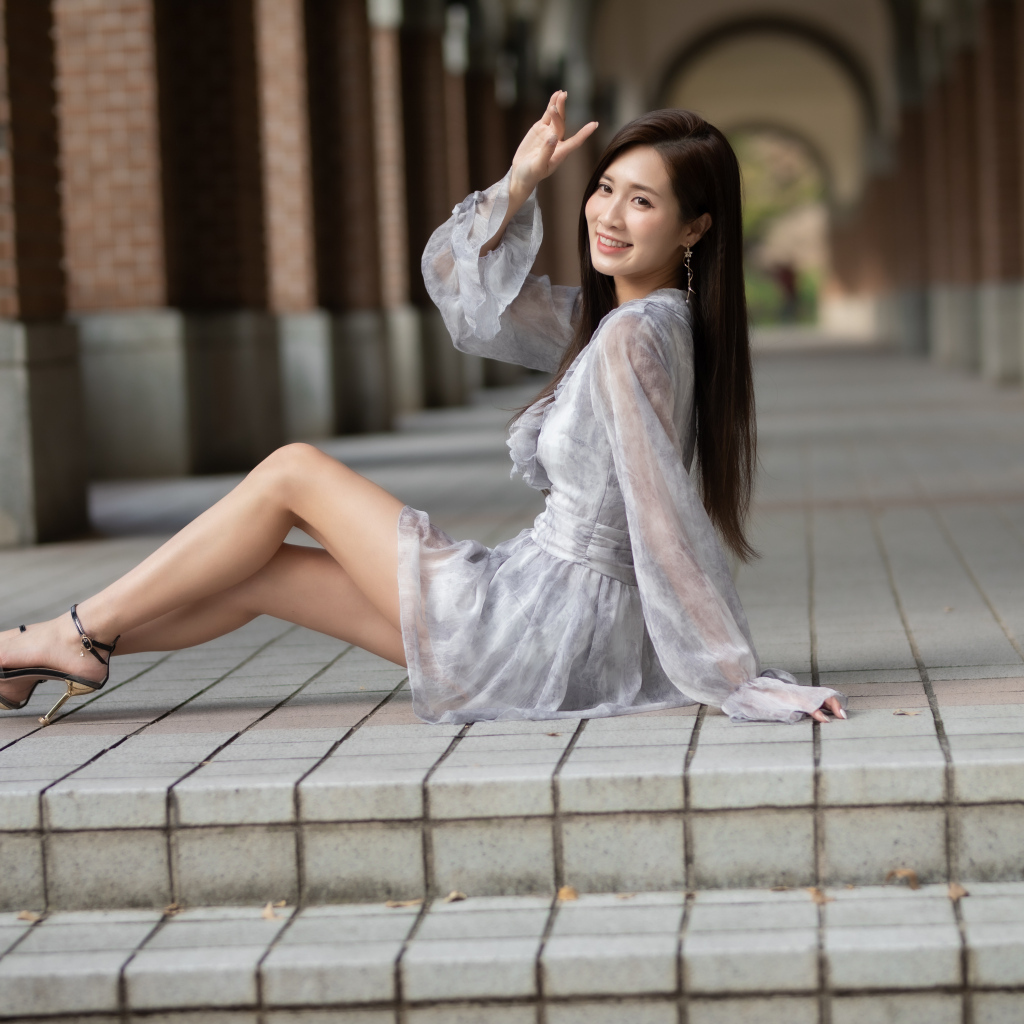 Улыбающаяся девушка азиатка сидит у ступеней