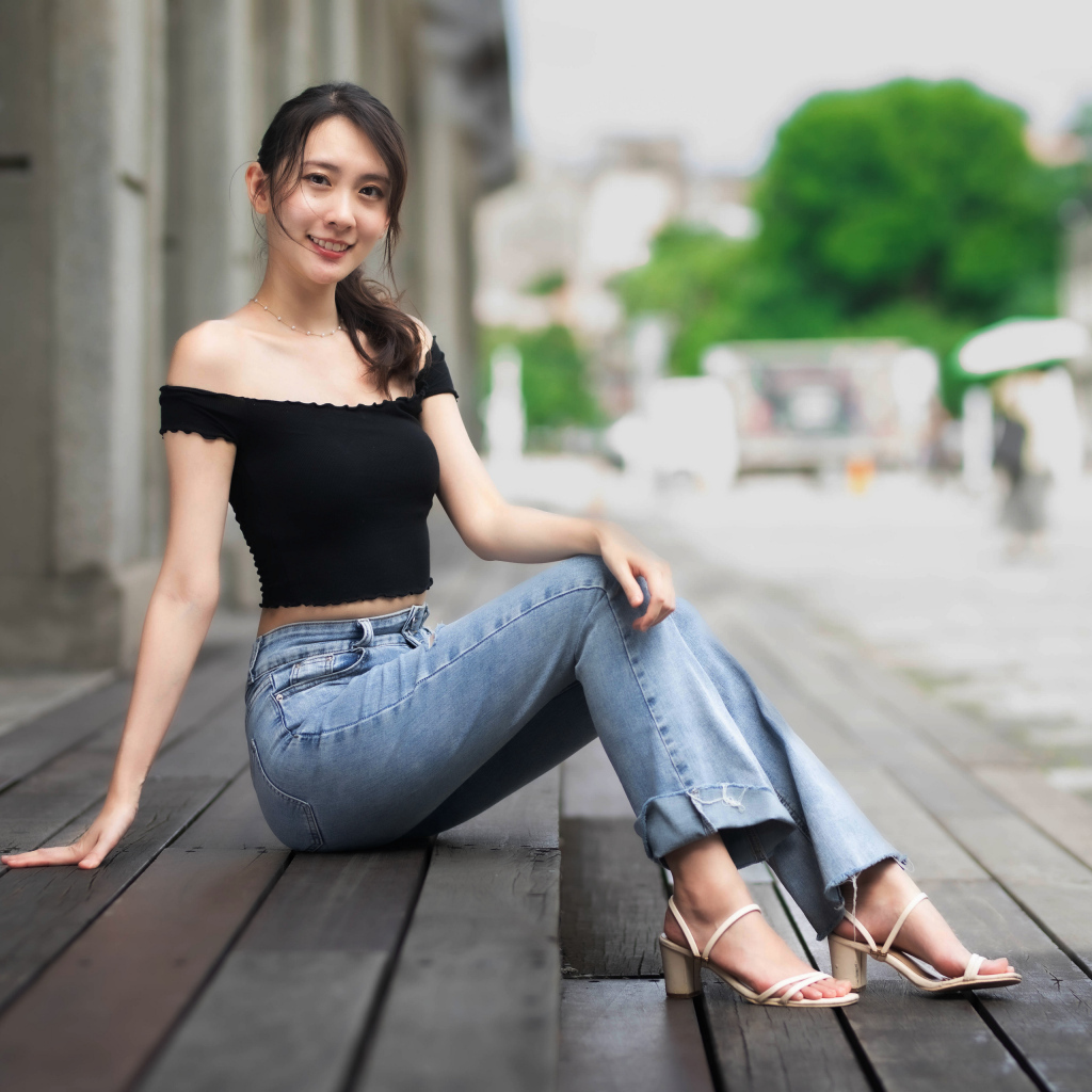 Улыбающаяся азиатка в джинсах сидит на пороге