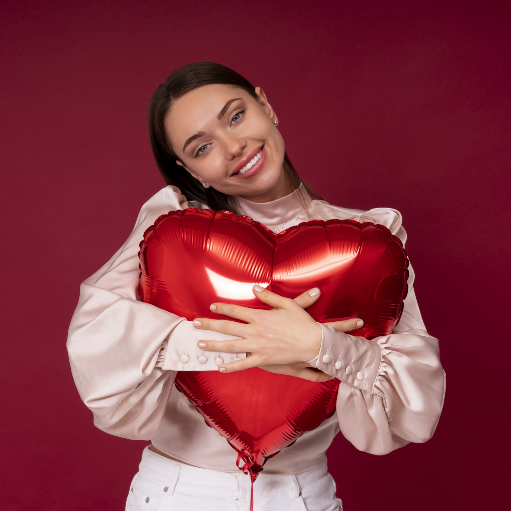 Улыбающаяся девушка обнимает шар в форме сердца