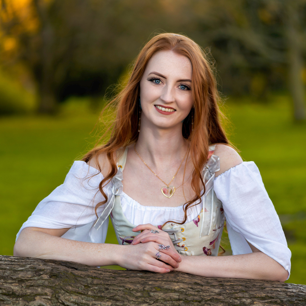 Улыбающаяся рыжеволосая девушка стоит у дерева