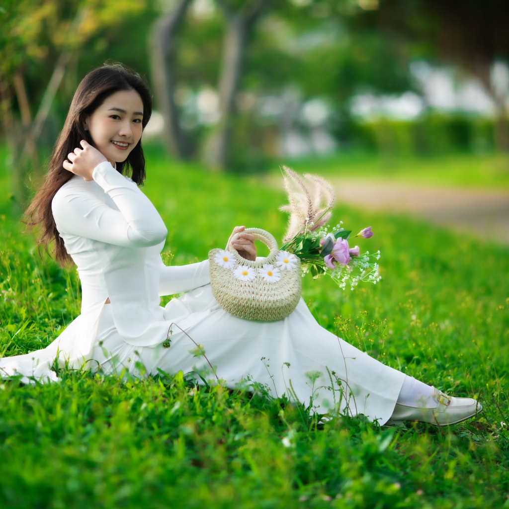 Нежная азиатка в белом наряде сидит на траве