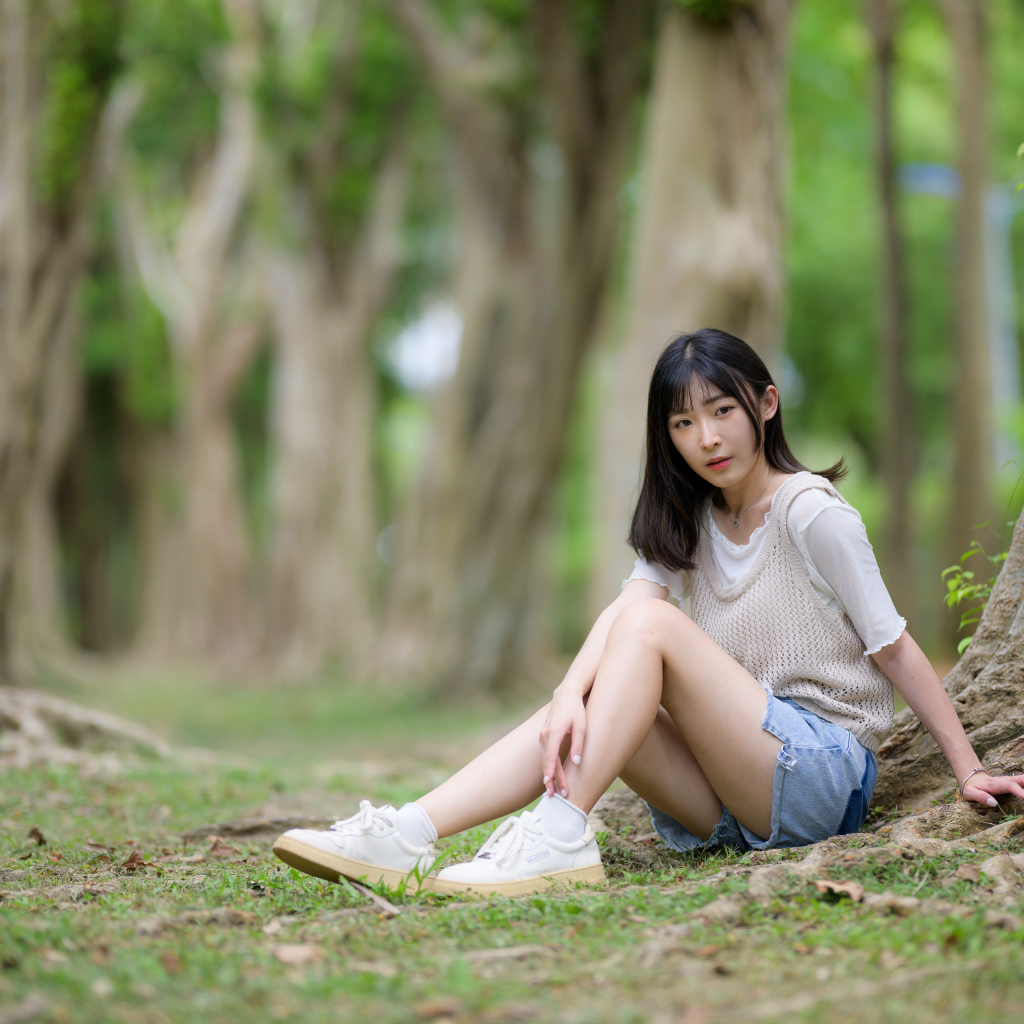 Молодая девушка азиатка сидит у дерева в парке
