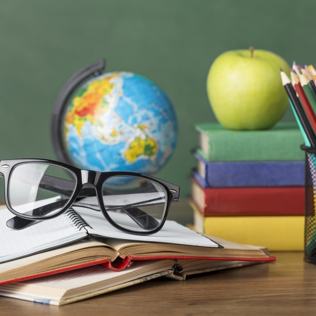 Книги, очки и карандаши с глобусом на столе у доски