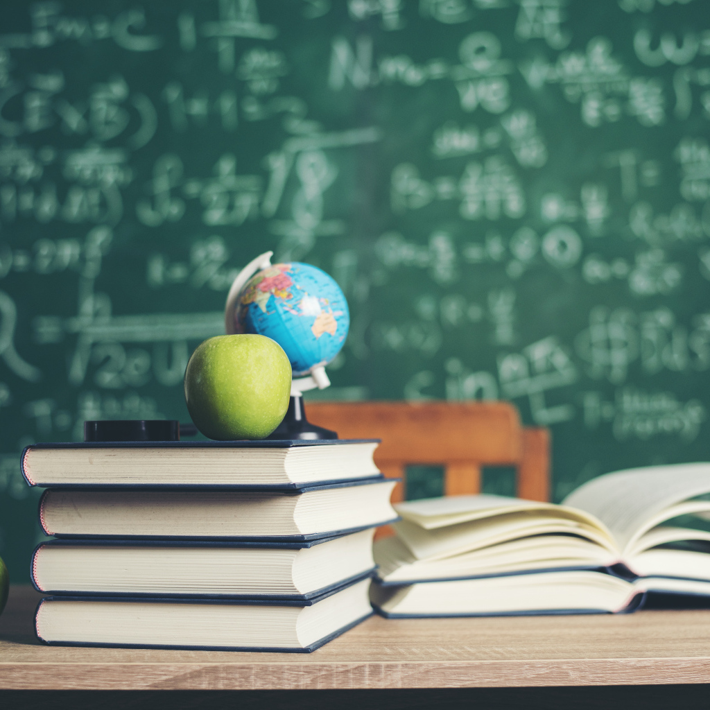 Книги на столе с зелеными яблоками и глобусом на фоне доски