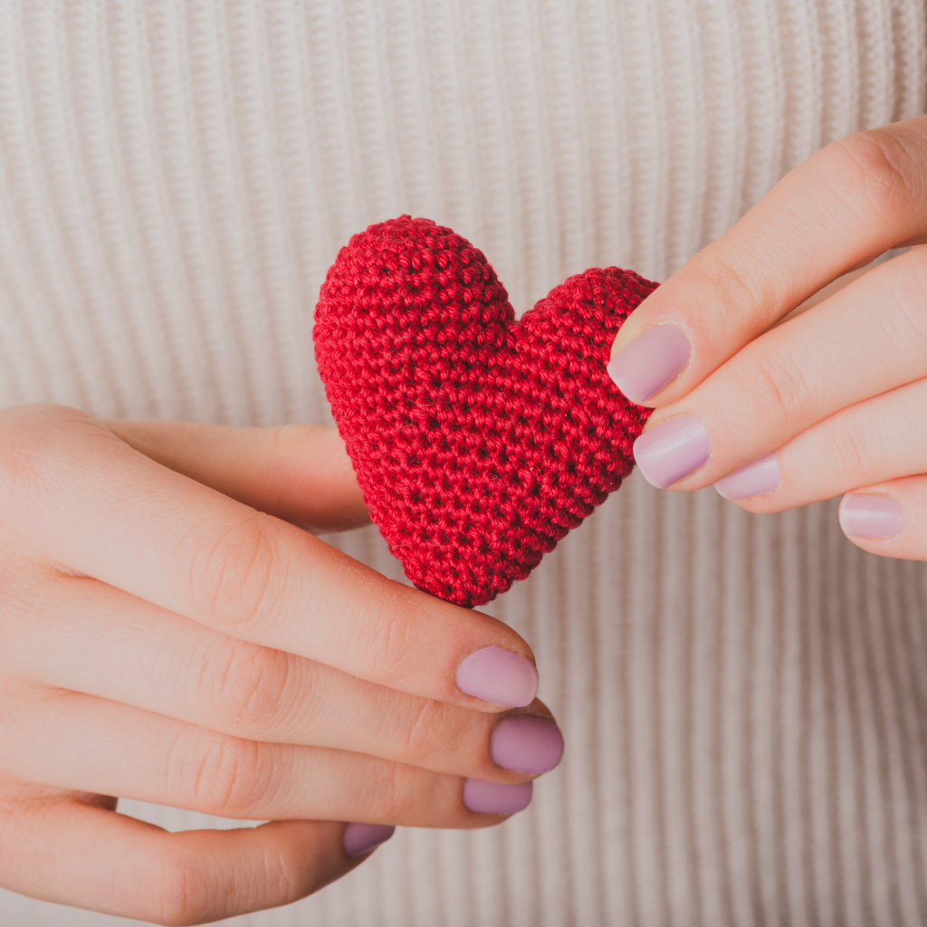 Девушка держит в руке вязаное красное сердце
