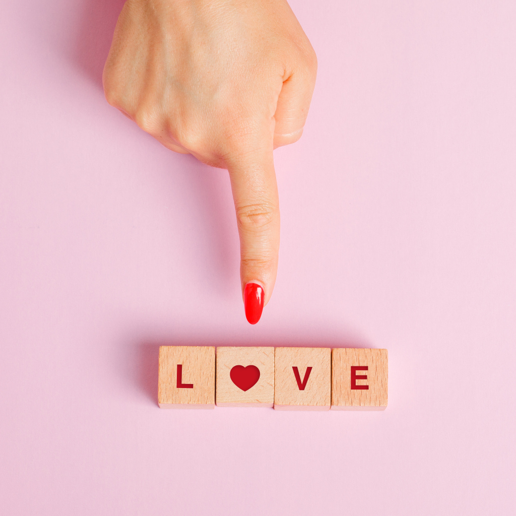 Рука указывает на кубики с надписью любовь на розовом фоне