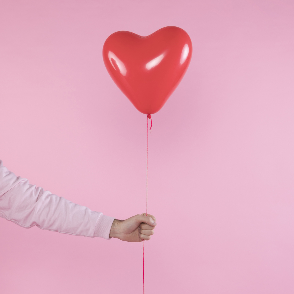 Шарик в форме сердца в руке на розовом фоне