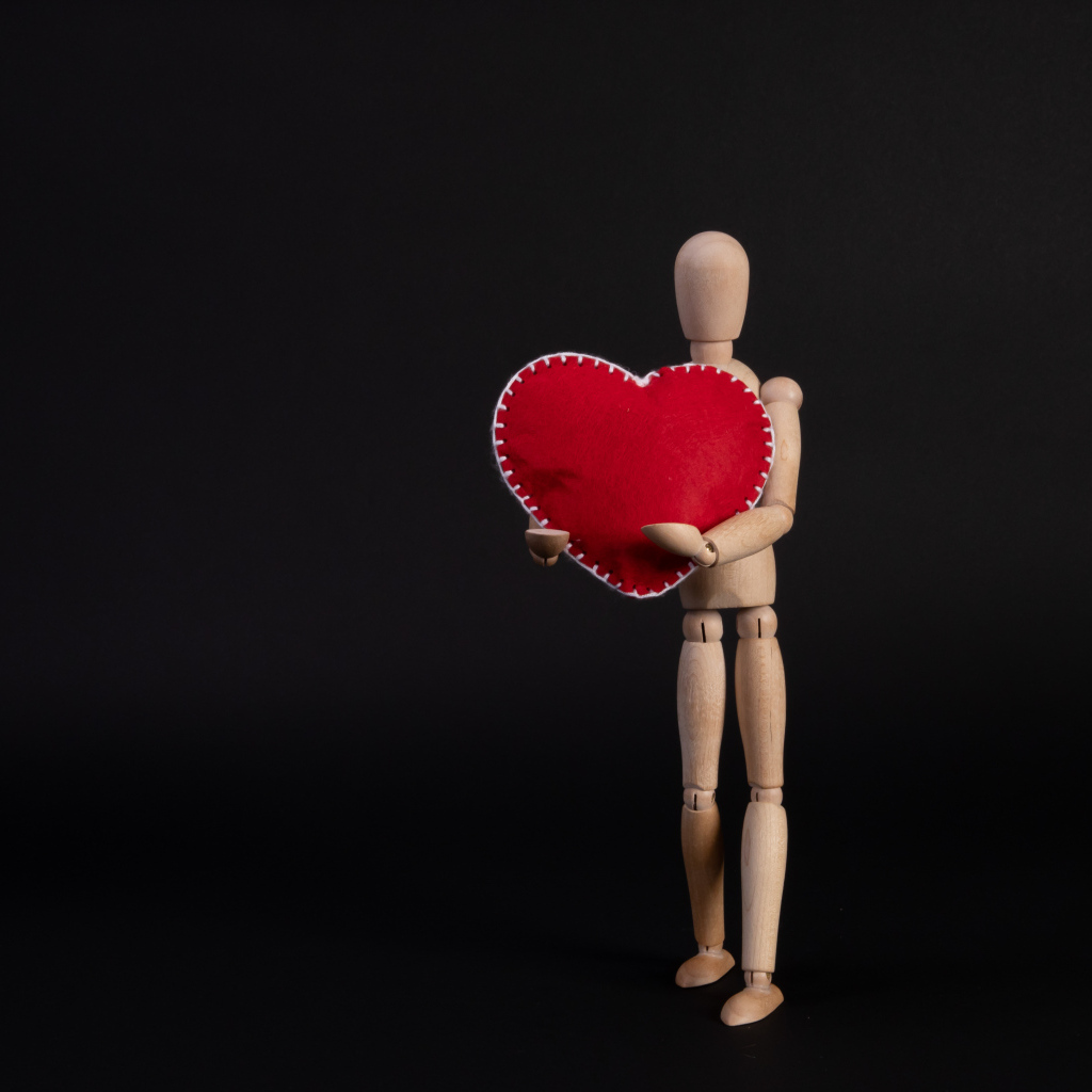Марионетка держит красное сердце на черном фоне
