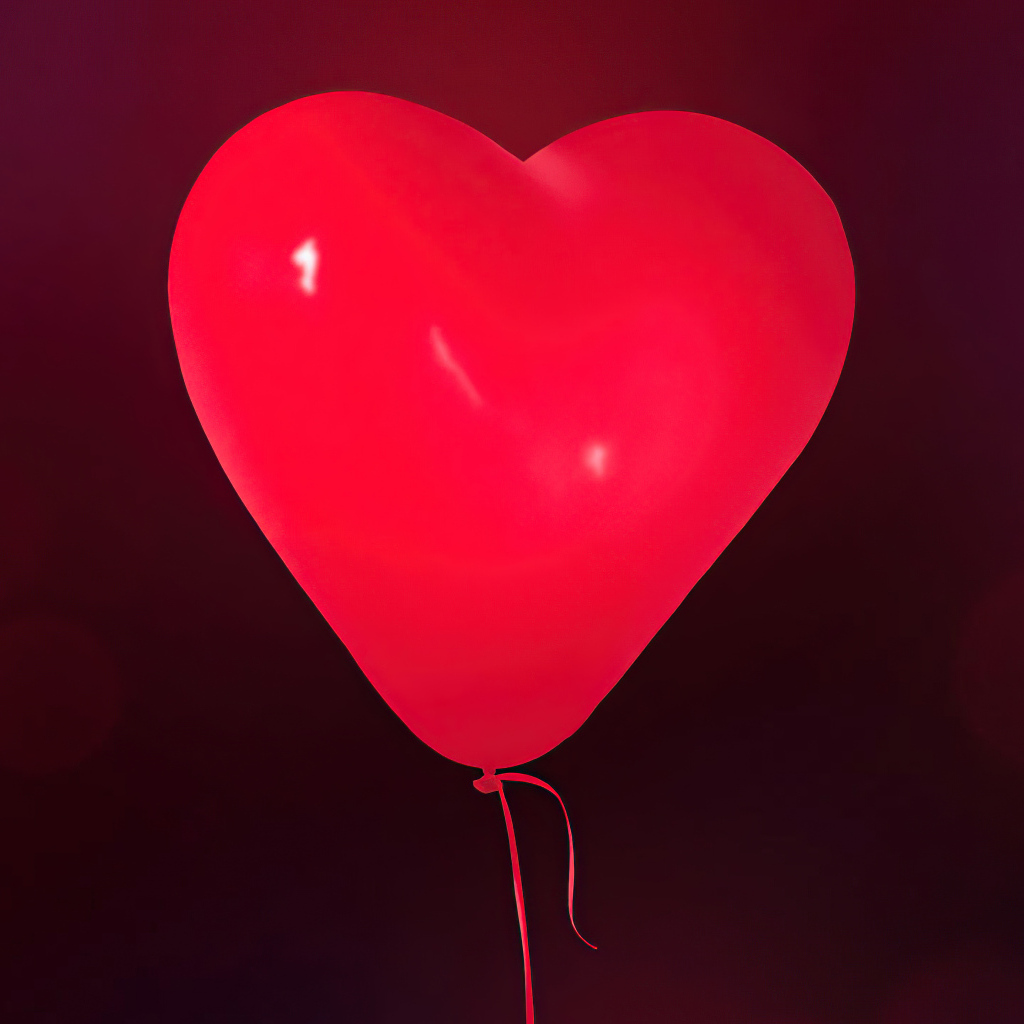 Красный шарик в форме сердца на фоне стены