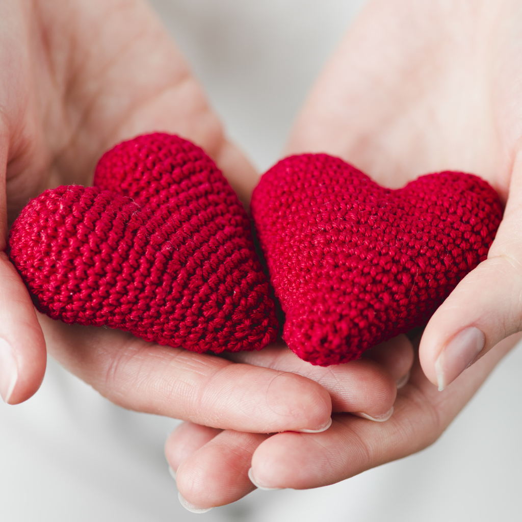 Два красных вязаных сердечка в руках девушки