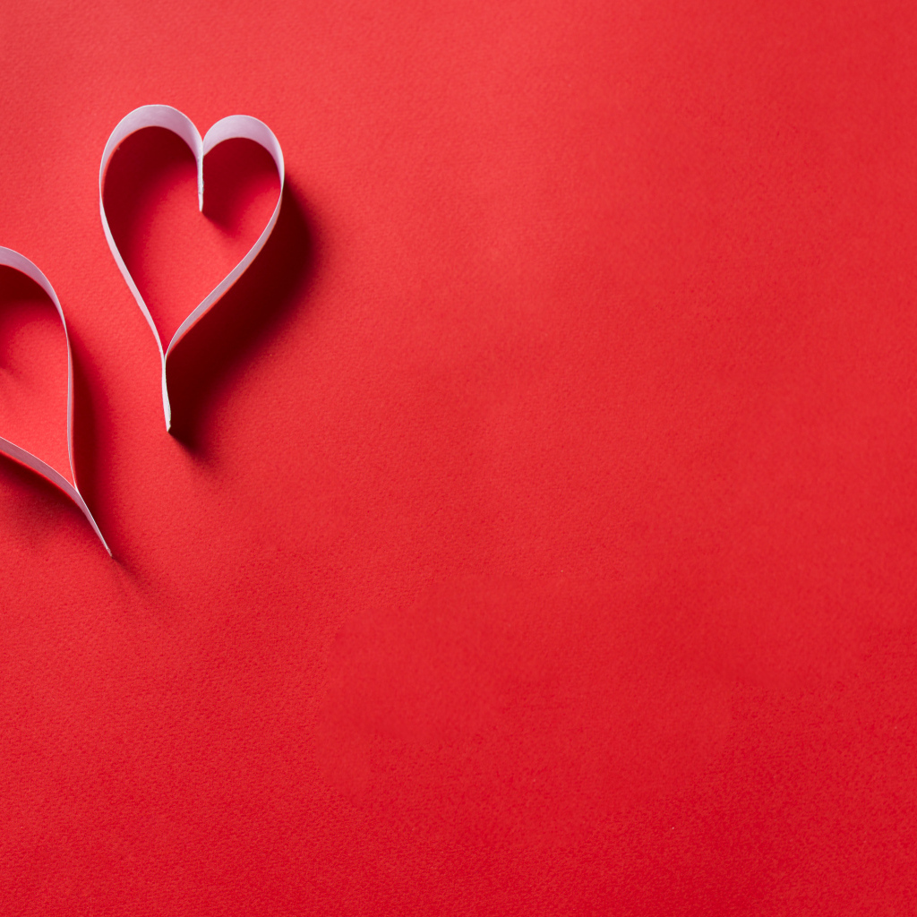 Два белых бумажных сердца на красном фоне
