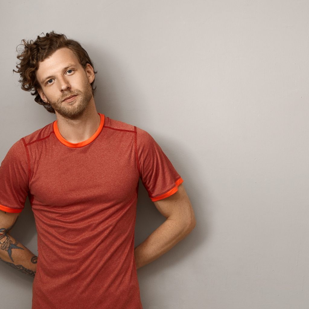 Мужчина в футболке стоит у серой стены