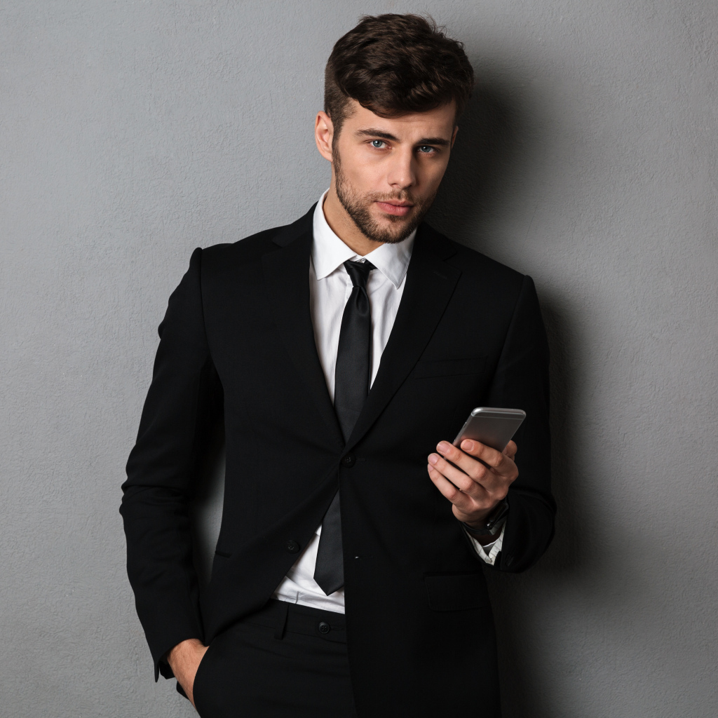 Деловой мужчина в костюме стоит у стены с телефоном