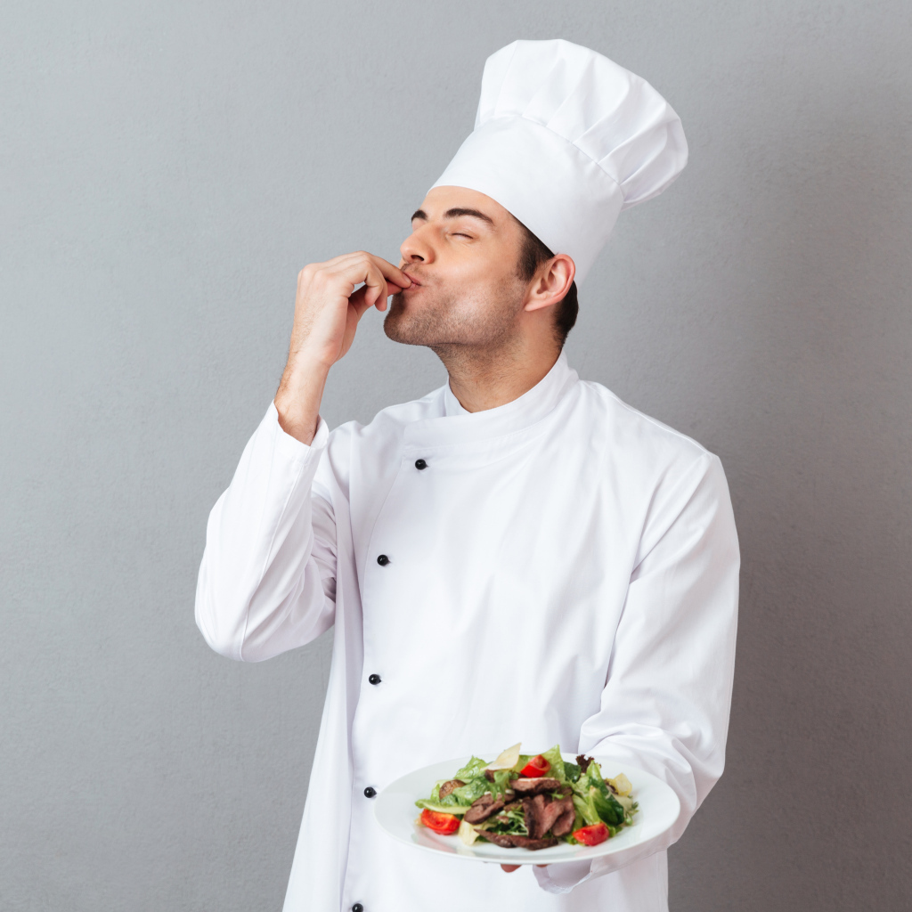 Мужчина повар в белом костюме с блюдом на сером фоне
