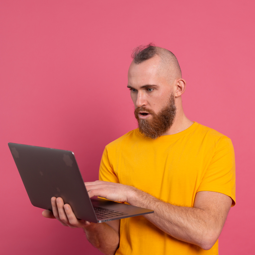 Удивленный мужчина с ноутбуком на розовом фоне