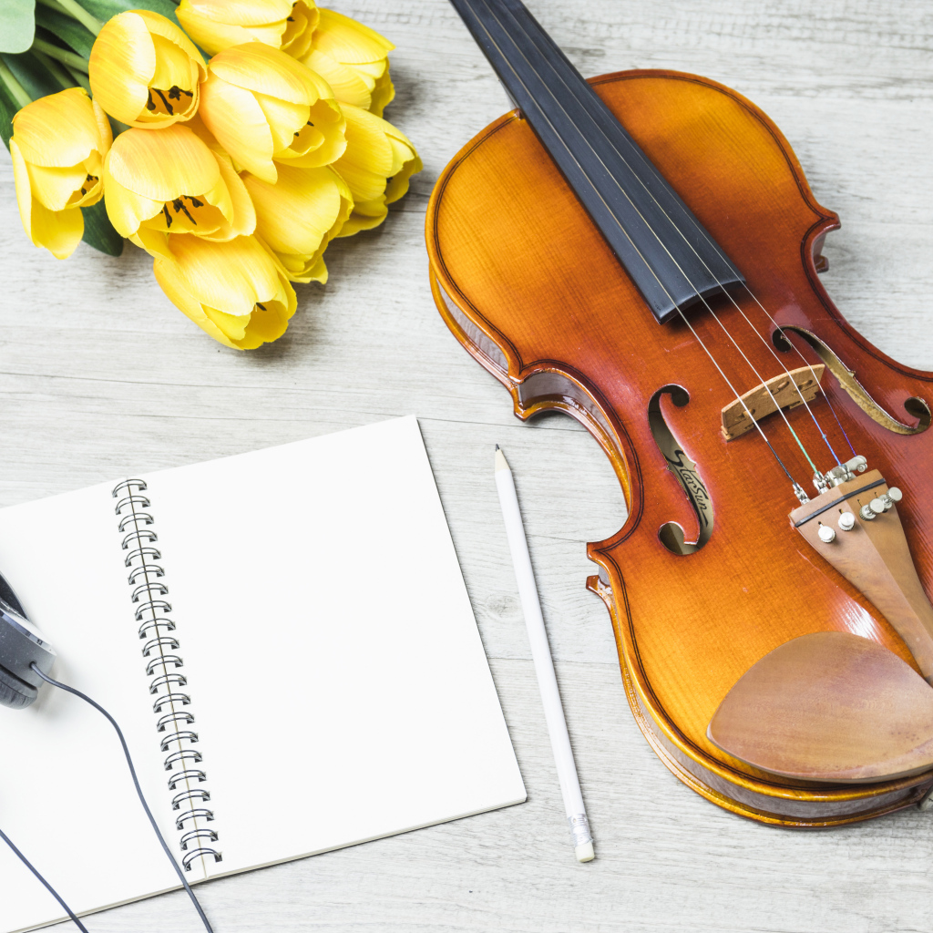 Красивая скрипка на столе с блокнотом, наушниками и букетом тюльпанов