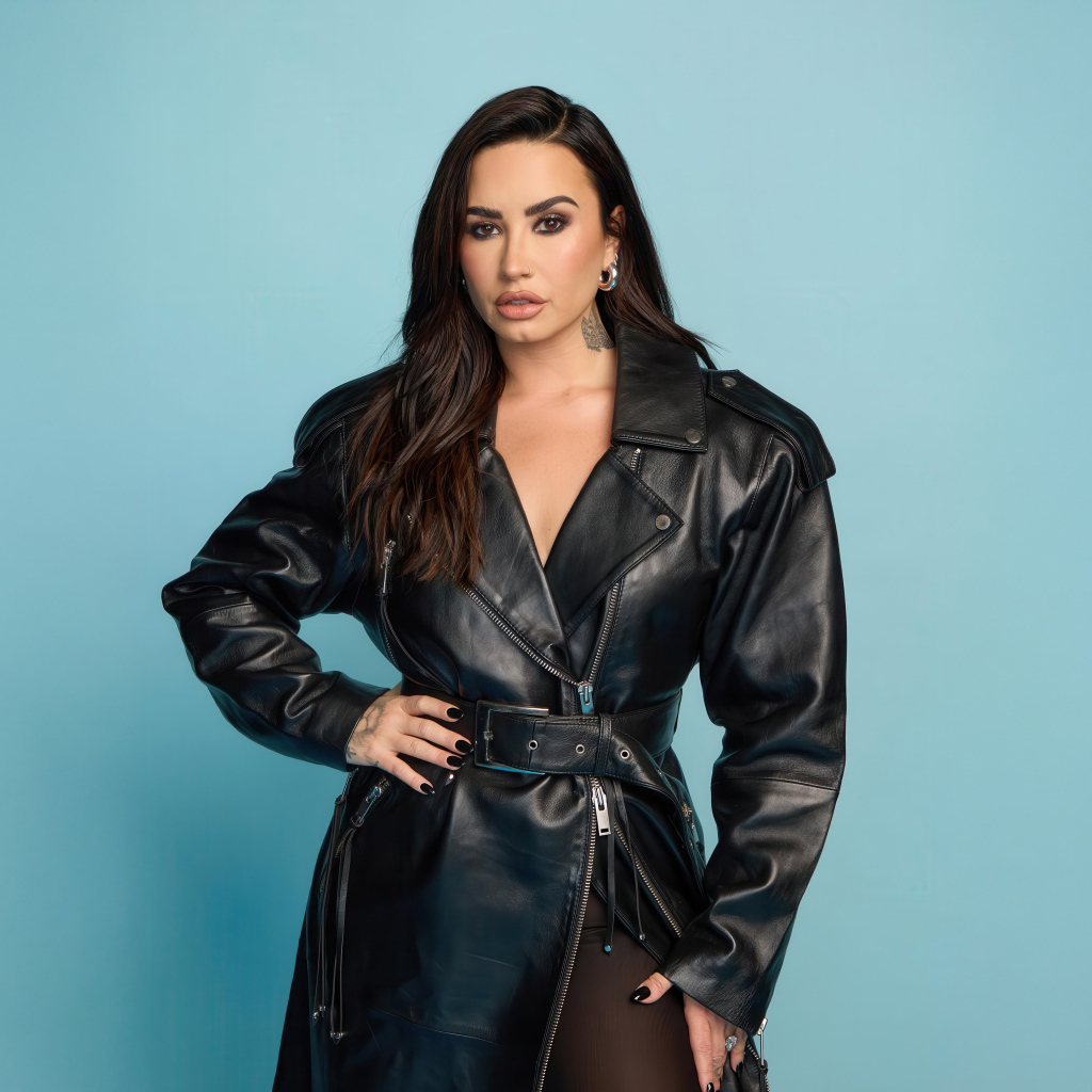 Певица Деми Ловато в кожаном черном пальто на голубом фоне