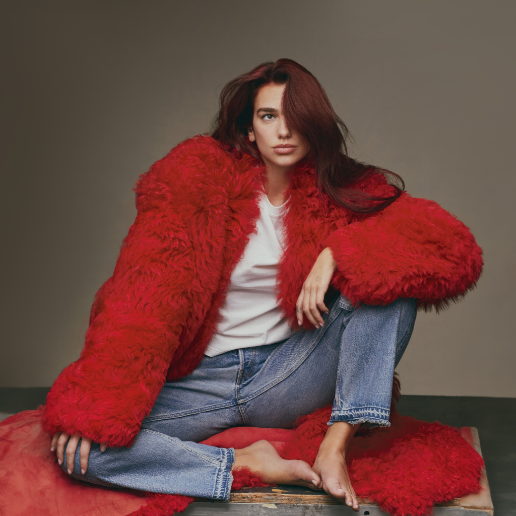 Певица Дуа Липа в красной шубе сидит на полу