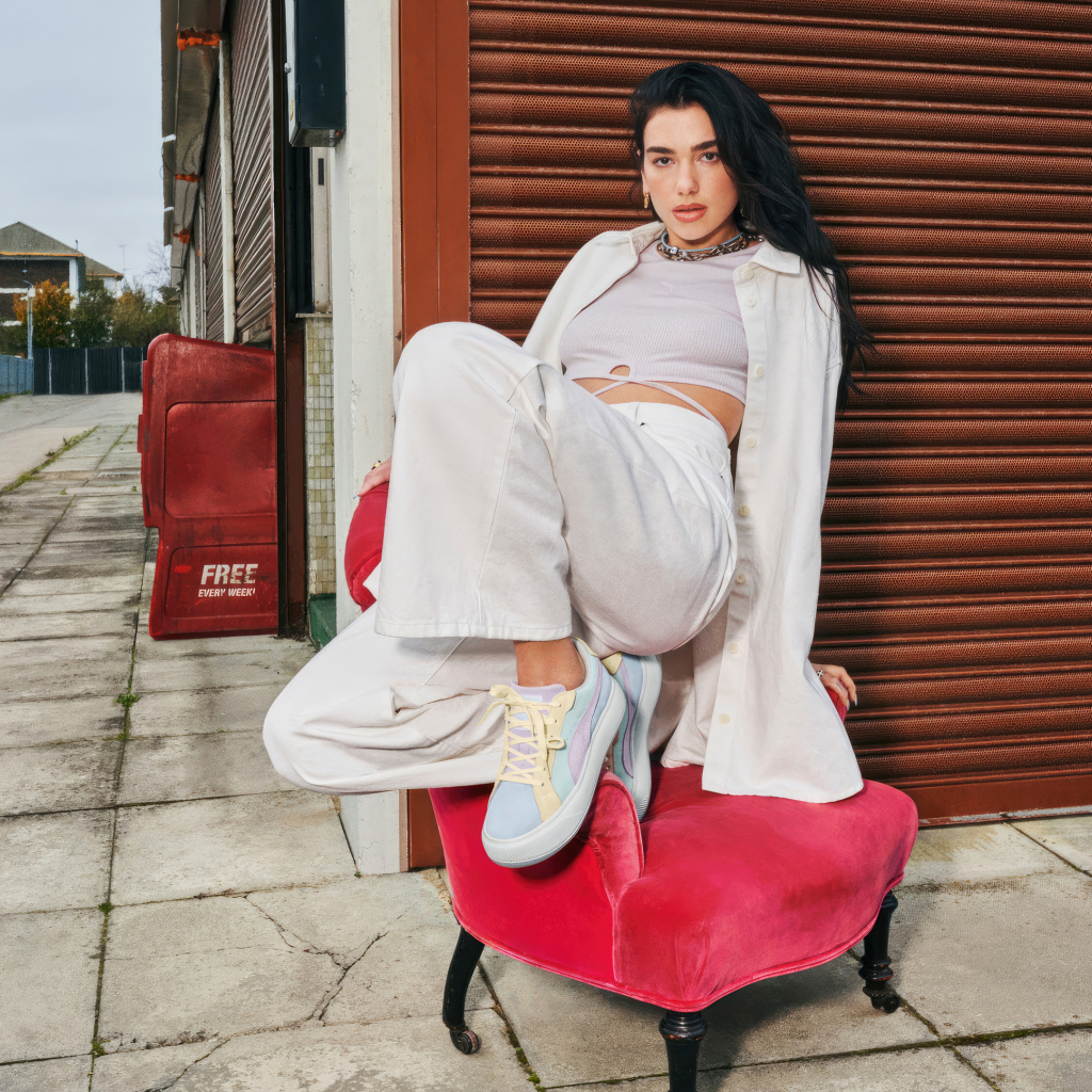 Певица Дуа Липа в белом костюме на кресле у стены