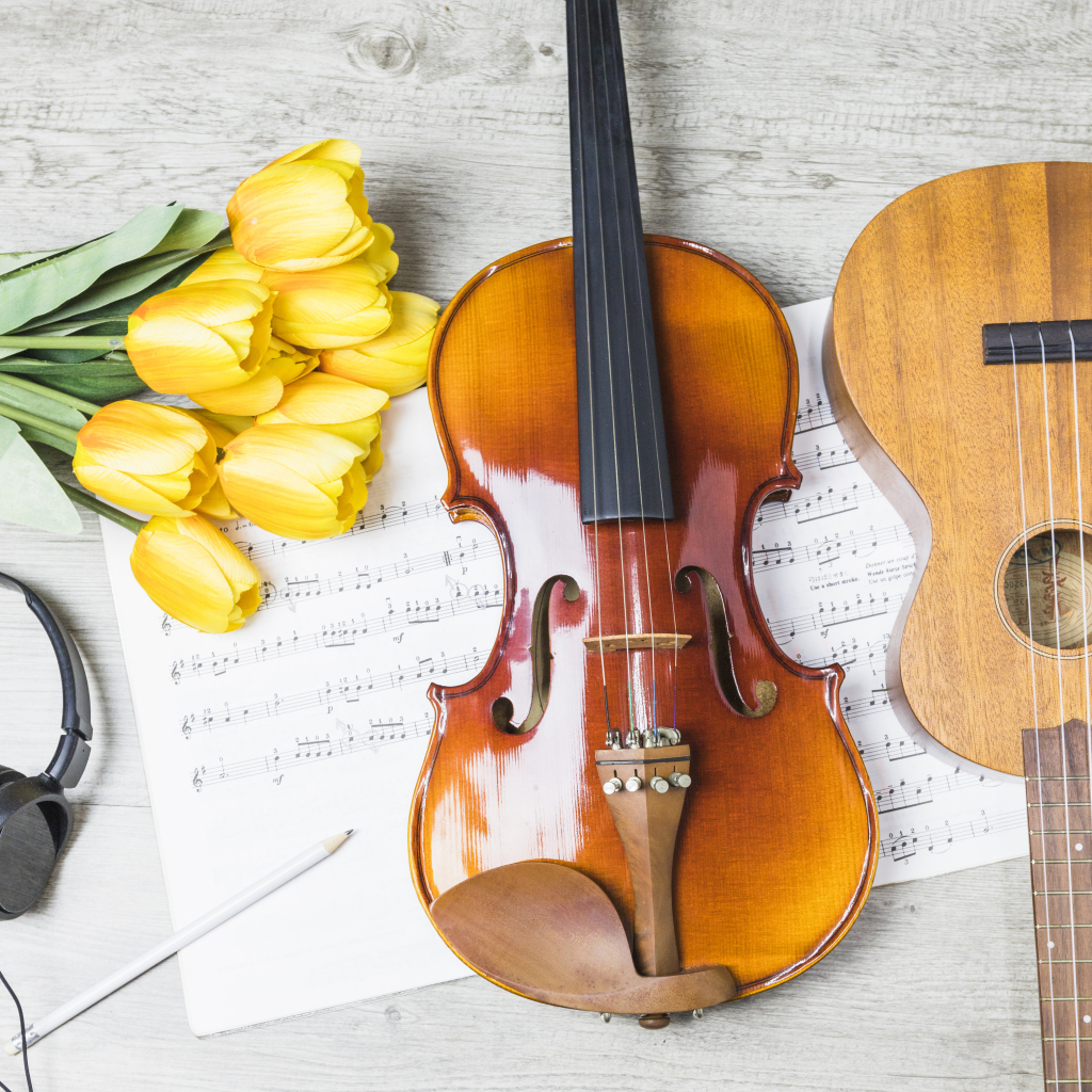 Маленькая гитара и скрипка на столе с нотами, наушниками и букетом тюльпанов