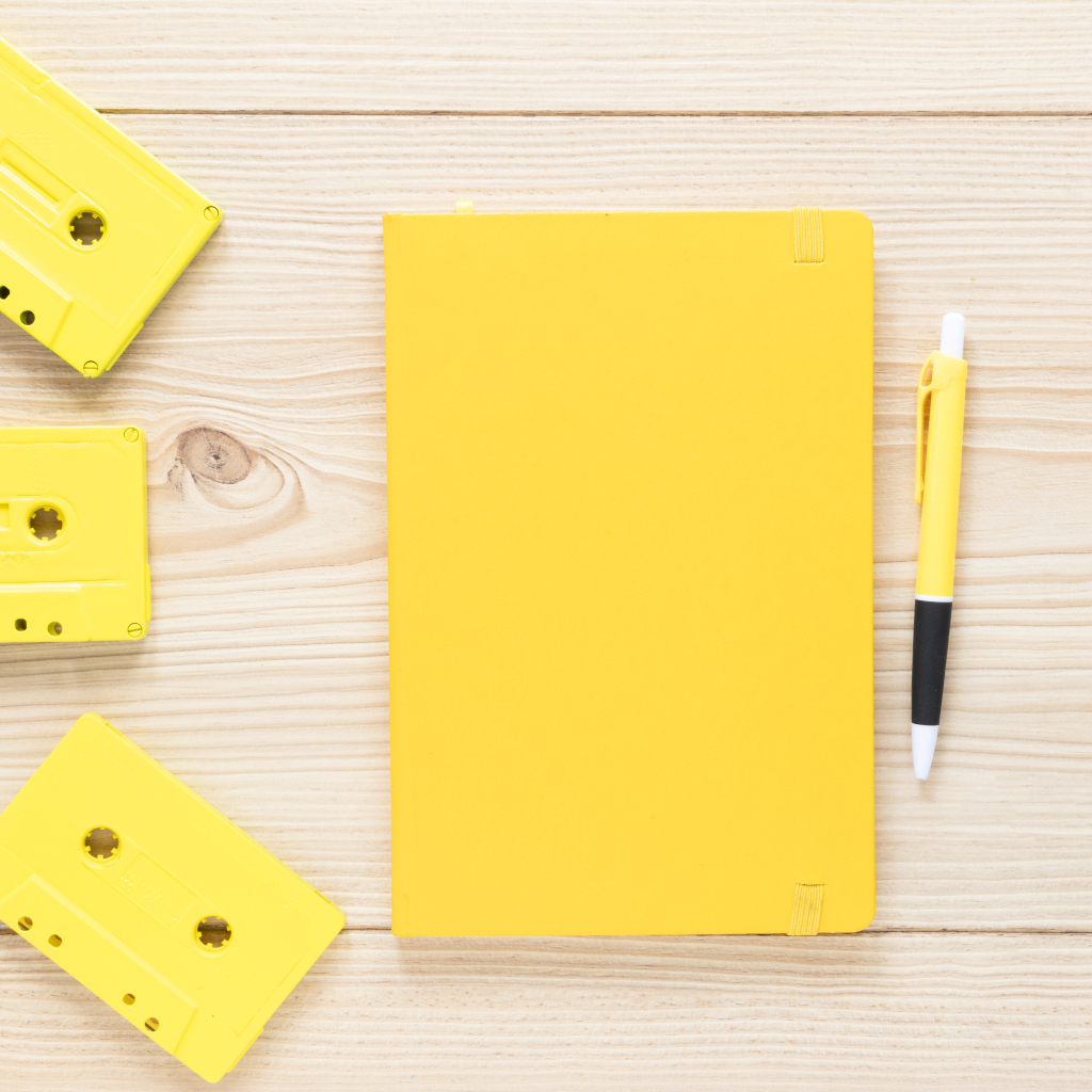 Желтый блокнот с ручкой и кассетами на столе
