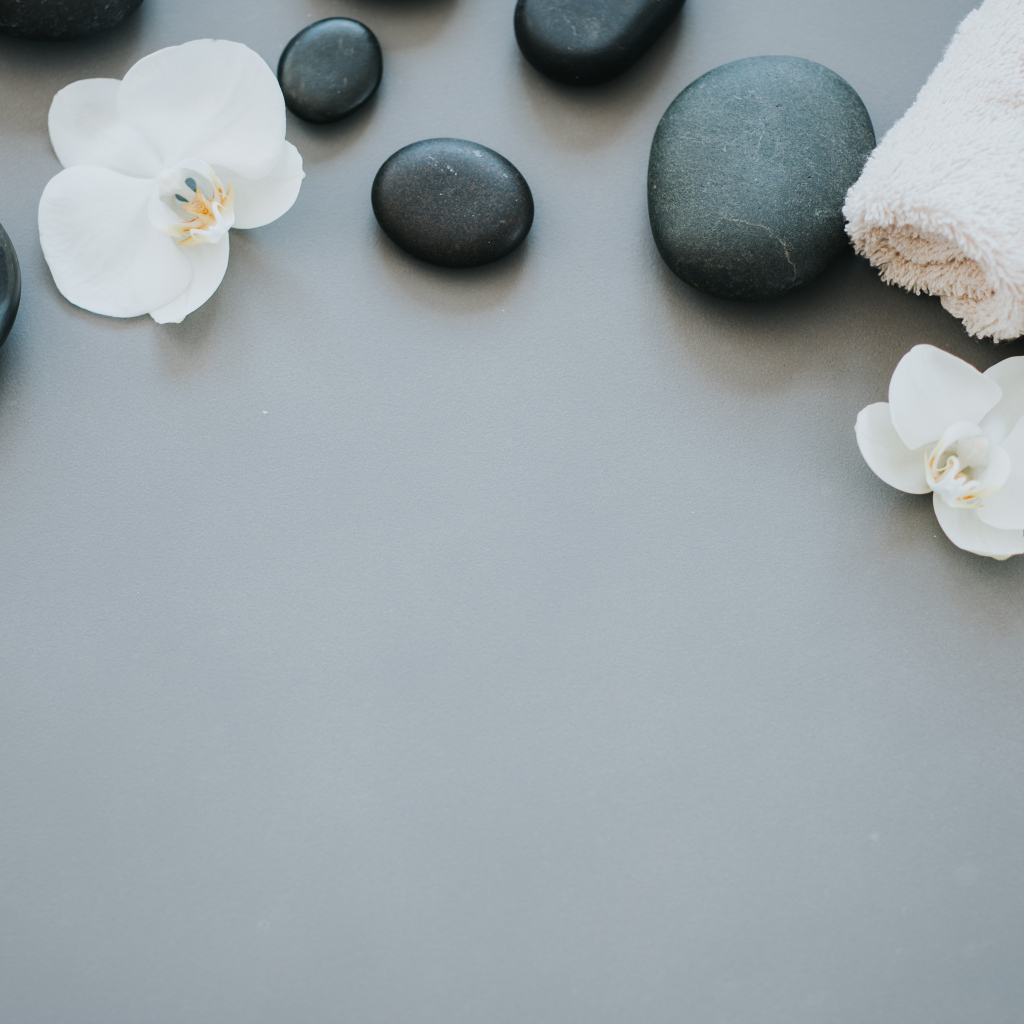 Черные камни с цветами орхидеи и полотенцем на сером фоне