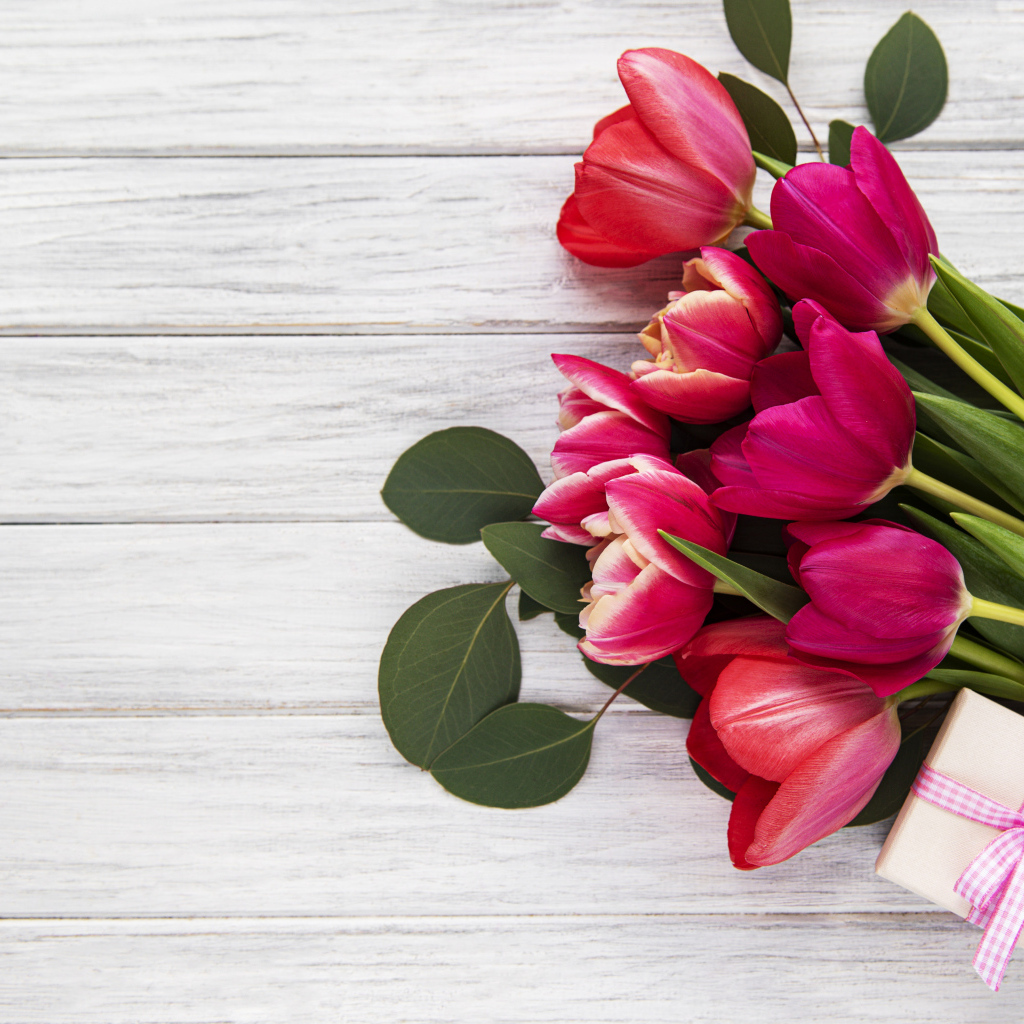 Букет розовых тюльпанов с подарком и зелеными листьями на белом столе