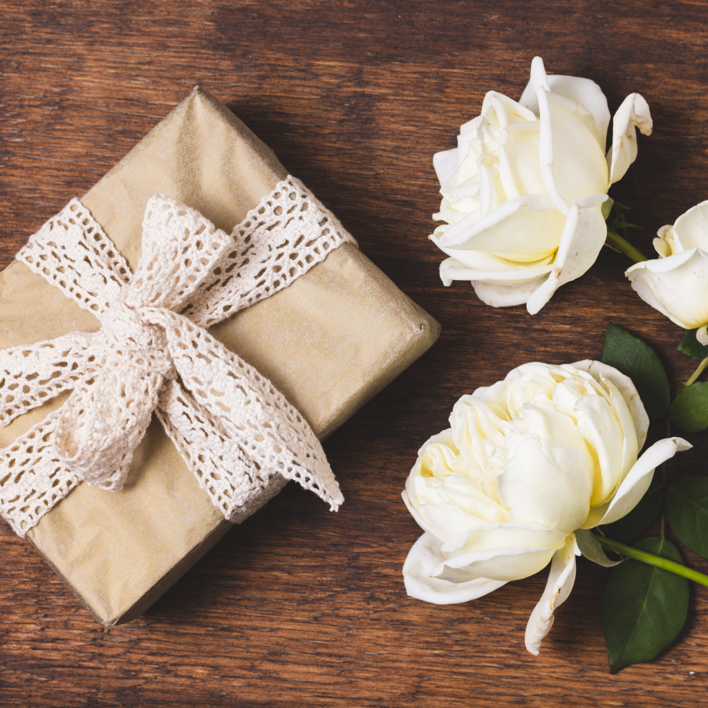 Коробка с подарком на деревянном столе с белыми розами