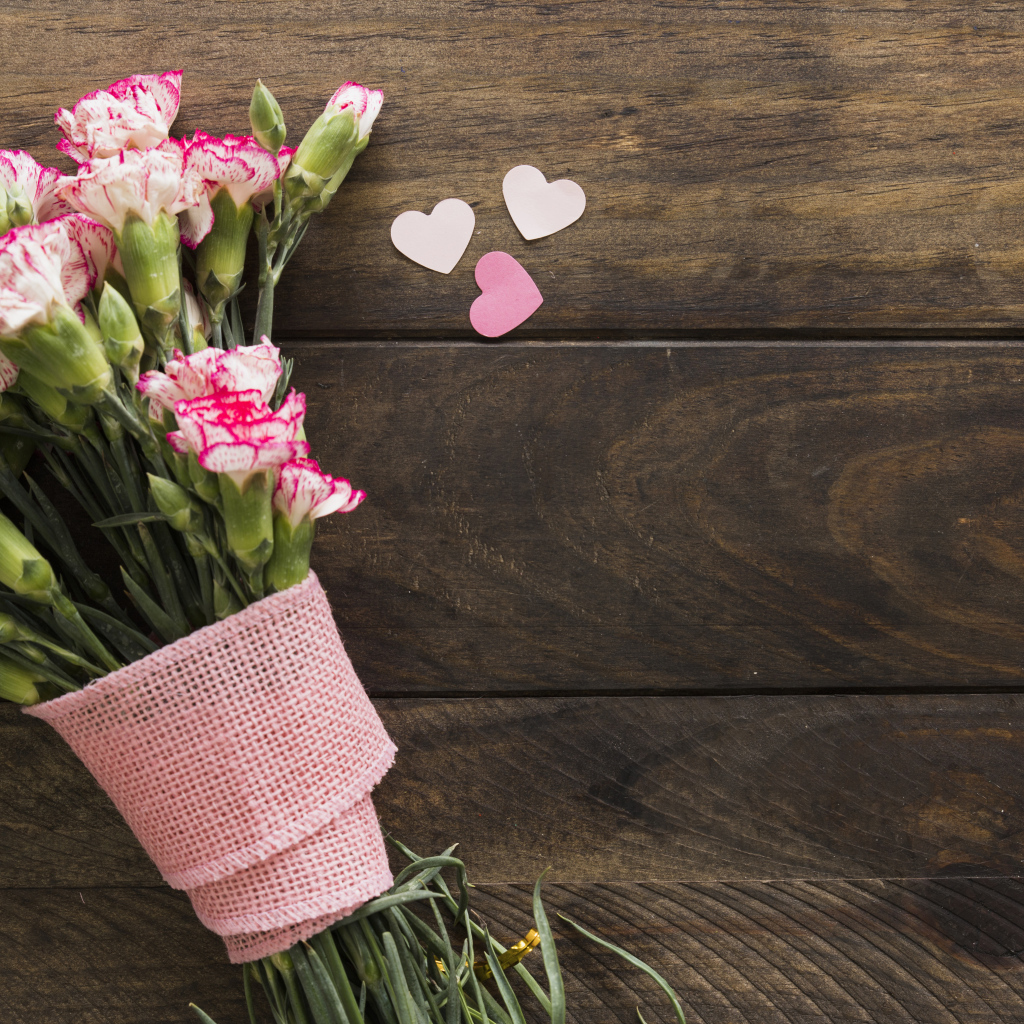 Розовые гвоздики с сердечками на коричневом деревянном фоне