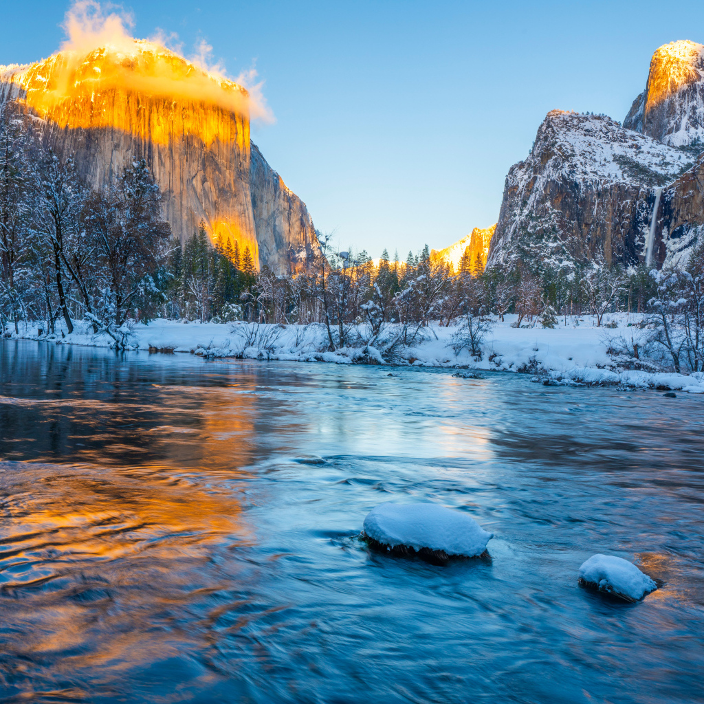 Холодная река с заснеженными берегами и горы в лучах солнца