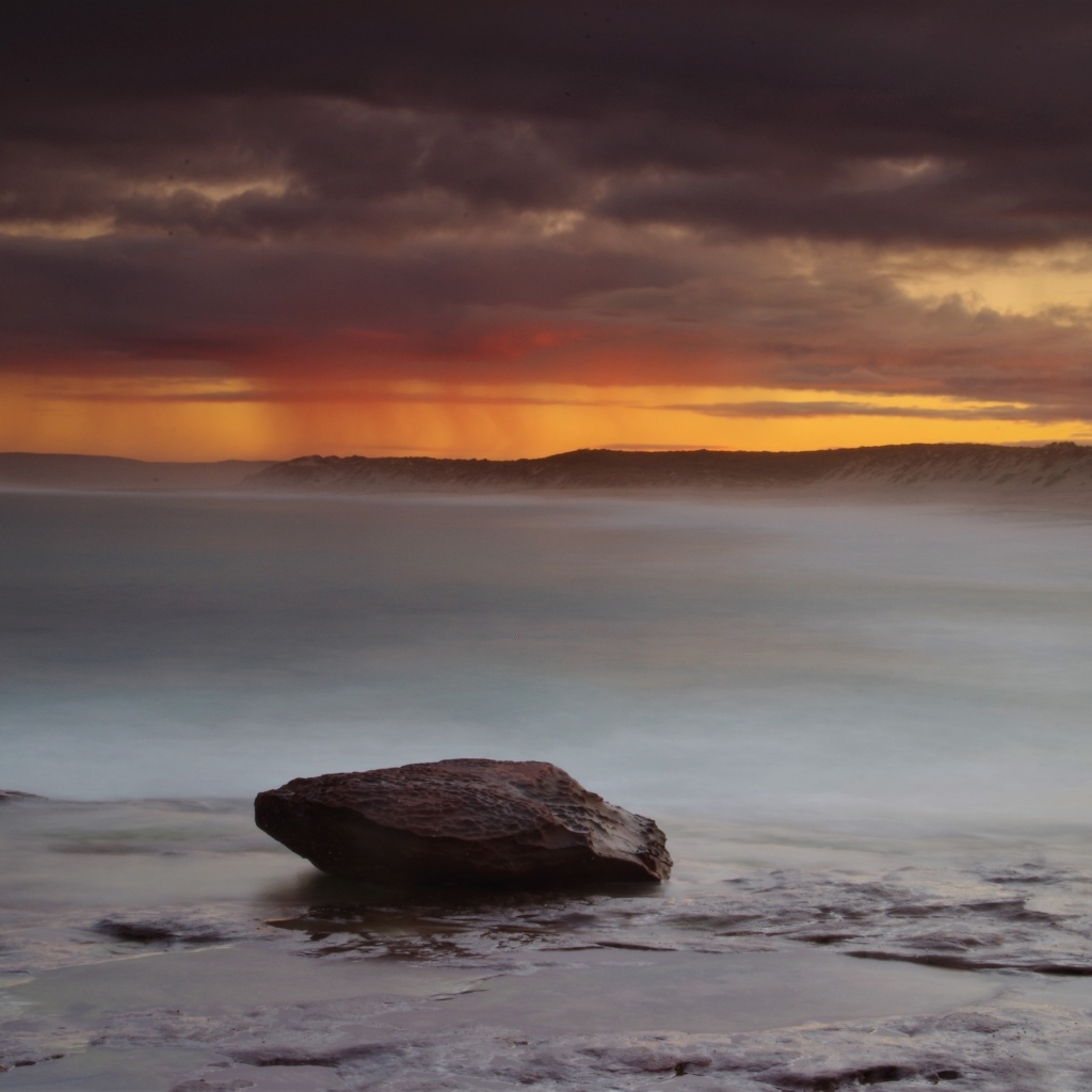 Большой камень в воде на фоне грозового неба в море