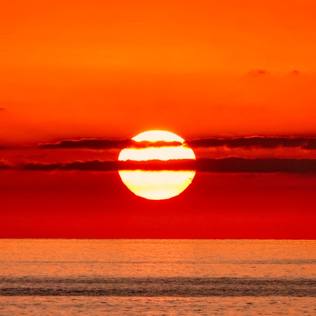 Яркое солнце в облаках на закате над морем 