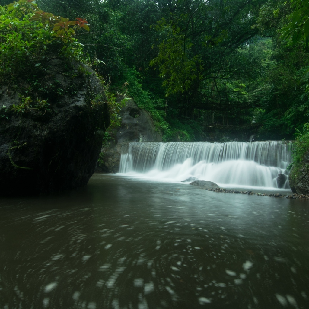 Водопад стекает в реку с большими камнями в лесу