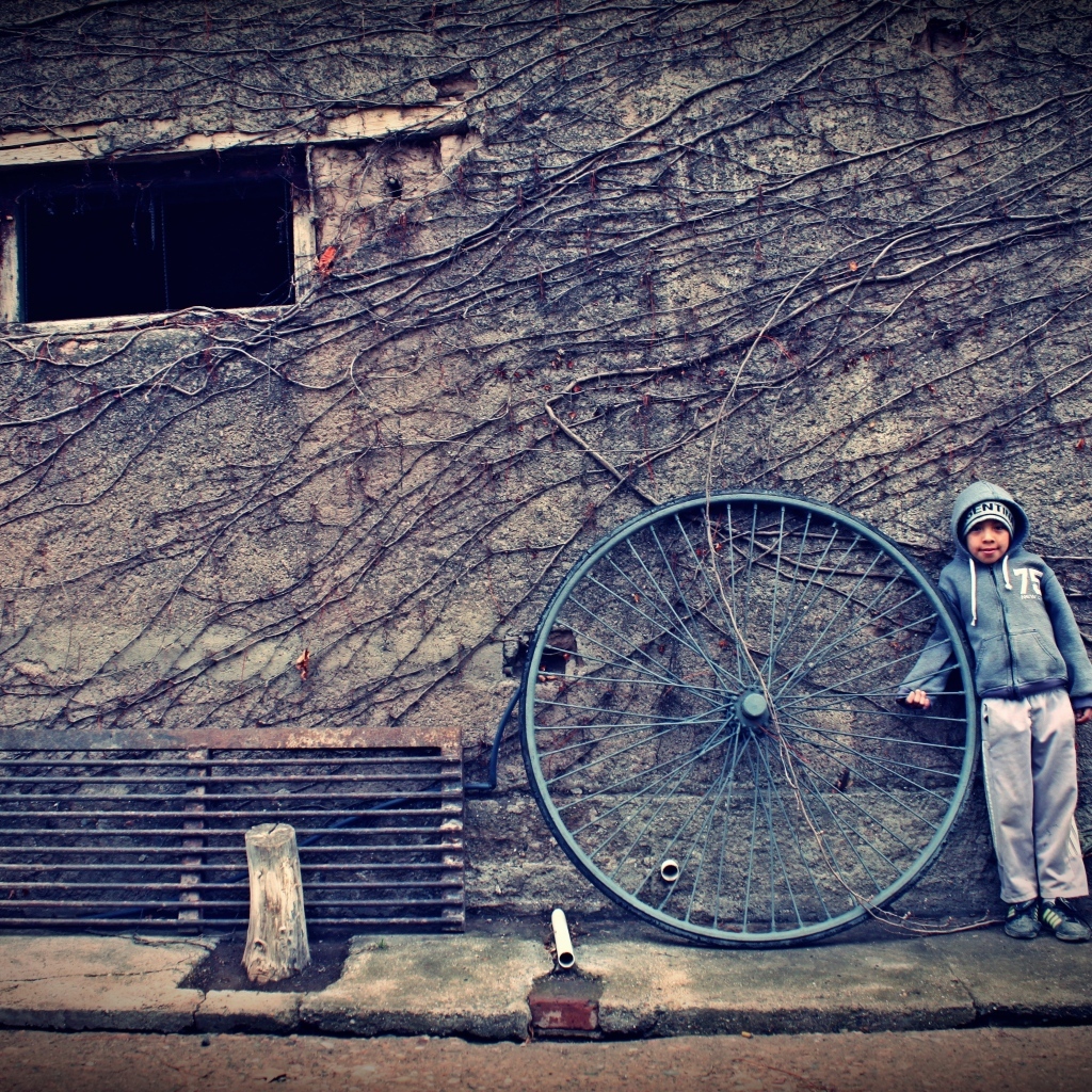 Мальчик с большим колесом стоит у стены