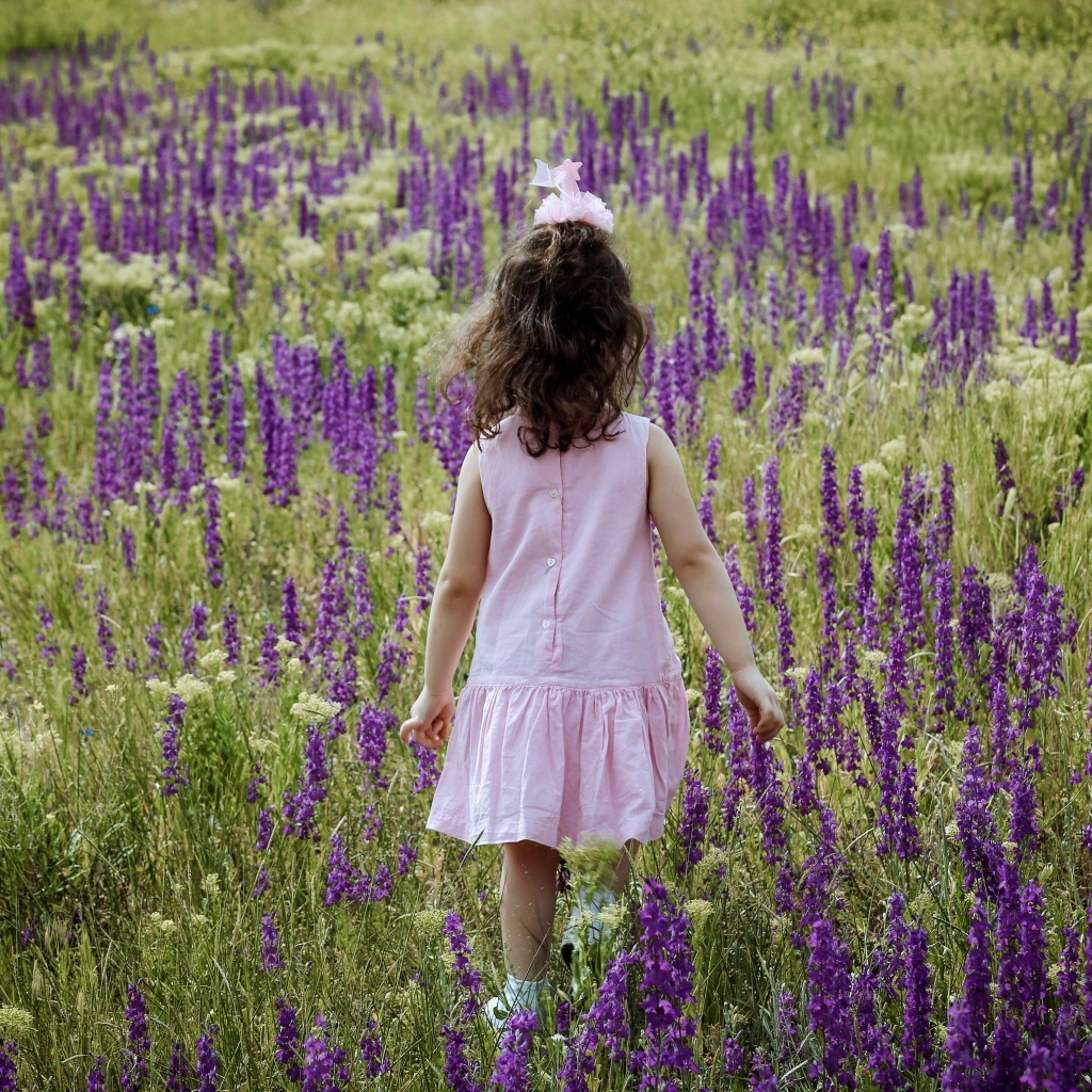 Девочка в розовом платье гуляет по полю с цветами