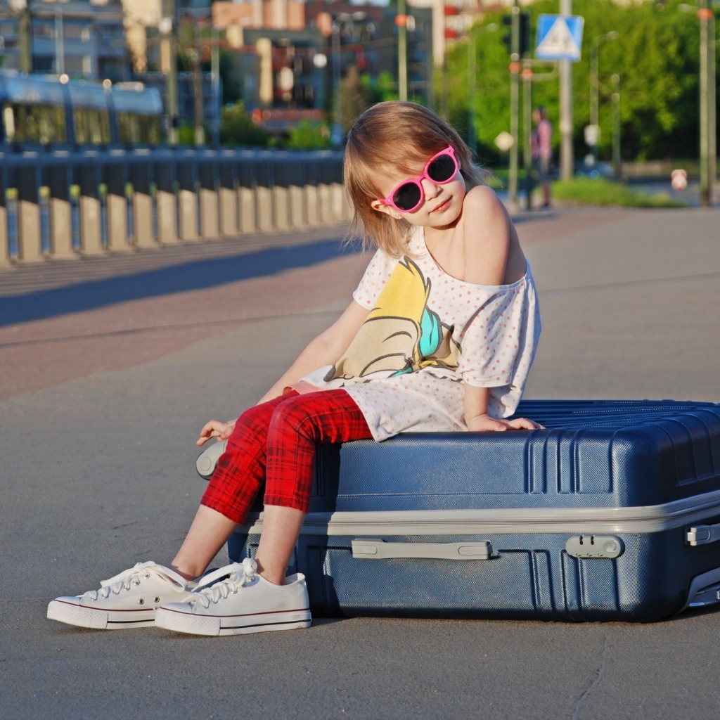 Девочка в солнечных очках сидит на чемодане на дороге