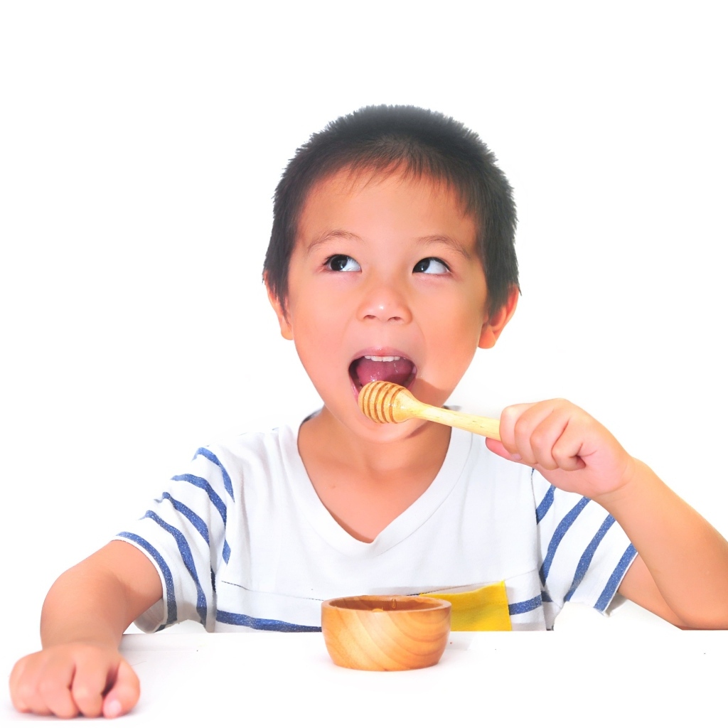 Мальчик азиат ест мед на сером фоне